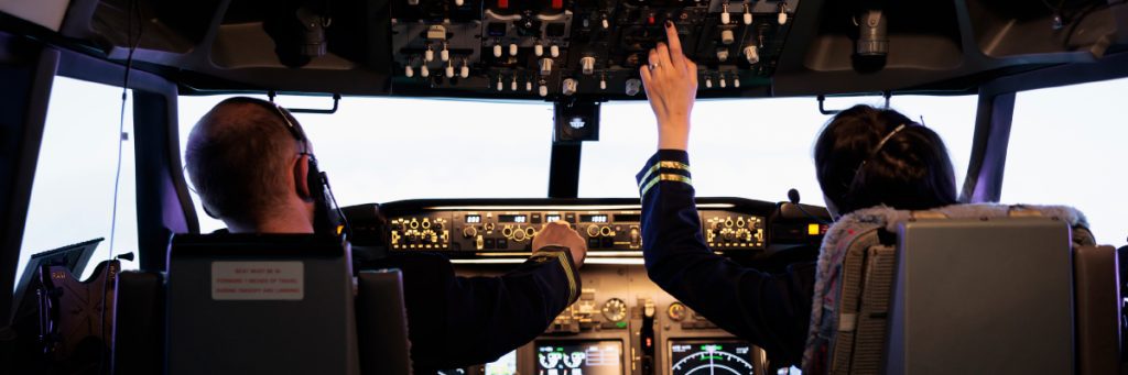 Vista desde la parte trasera de la cabina de un avión, con dos pilotos revisando los controles, en el artículo sobre quiénes deben realizar el curso de SMS