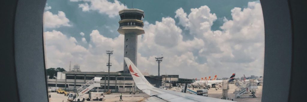 Torre de control de aeropuerto con un avión en la pista y cielo parcialmente nublado