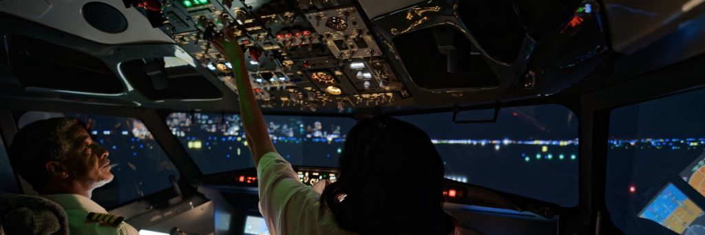 Primer plano de la cabina de un avión durante un vuelo nocturno, mostrando los controles mientras un piloto ajusta el panel, reflejando las mejoras en las condiciones de trabajo.
