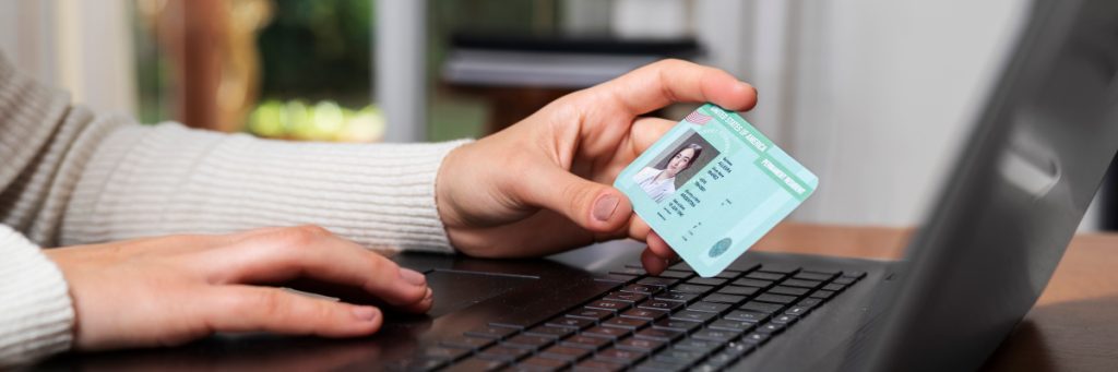 Persona sosteniendo su documento de identidad frente a una computadora portátil, completando el proceso de inscripción para la escuela de aviación en Bogotá.
