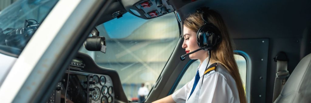 Mujer piloto operando los controles de la cabina de un avión, ilustrando las oportunidades de formación y cómo aprovechar la demanda de pilotos.