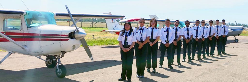 Grupo de estudiantes de aviación, hombres y mujeres, en formación frente a una avioneta de entrenamiento de Dream Fly, listos para iniciar su proceso de admisión.